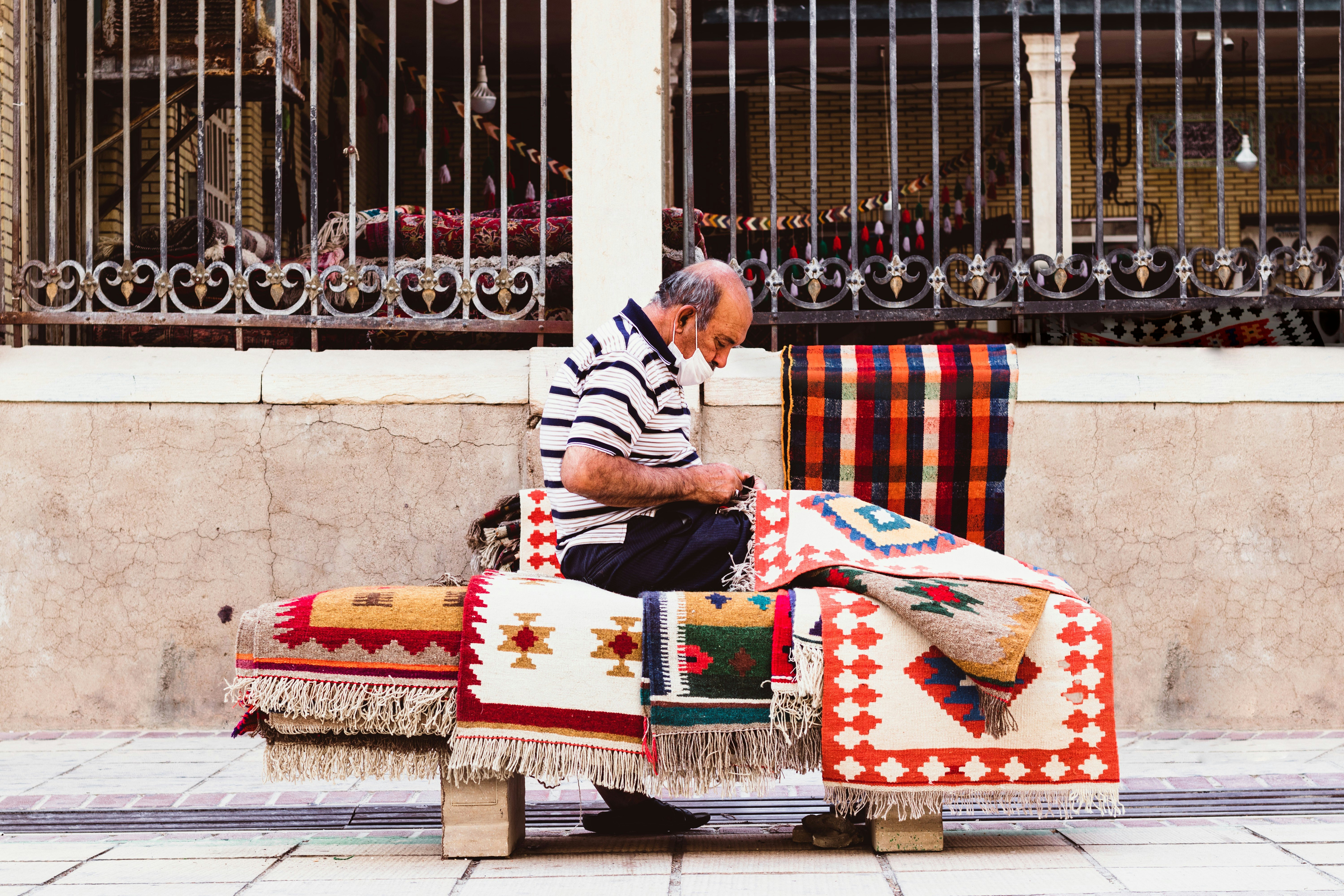 man in white and black stripe long sleeve shirt sitting on white red and blue textile